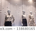 In the store window, there are three female mannequins dressed in clothes and hanging white light bulbs. 138680165