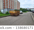 In the city courtyard, there is a huge rusty yellow garbage container for collecting construction waste. 138680171