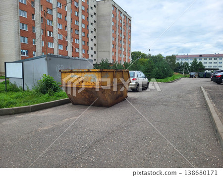 In the city courtyard, there is a huge rusty yellow garbage container for collecting construction waste. 138680171