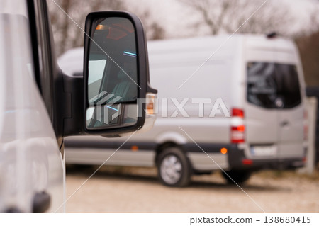 View of a white commercial van through a vehicle side mirror on a cloudy day in an outdoor setting. 138680415