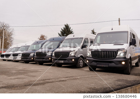 Row of modern white and dark grey commercial transport vans parked on an asphalt lot during overcast day. Row of modern white and dark grey commercial transport vans parked on an asphalt lot during overcast day. 138680446
