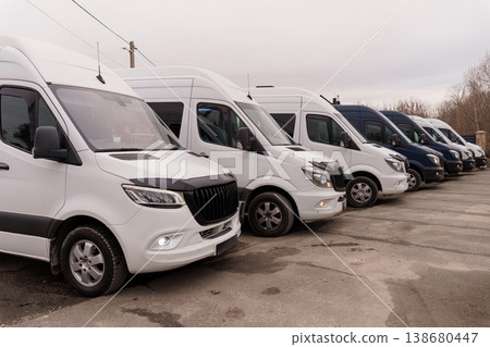 Row of white and dark delivery vans parked on asphalt lot under overcast sky in outdoor setting. Row of white and dark delivery vans parked on asphalt lot under overcast sky in outdoor setting. 138680447