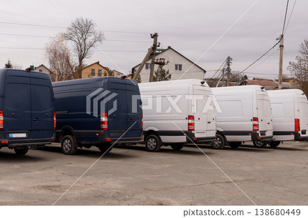 Row of blue and white commercial delivery vans parked in an outdoor lot near residential buildings. 138680449