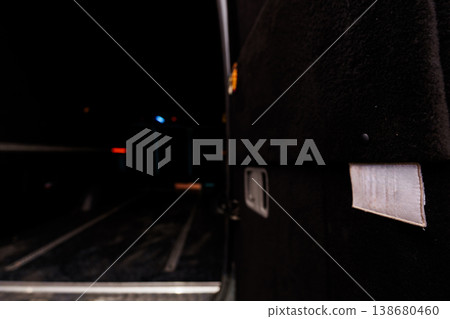 Close-up of black train side panel with reflective strip near dark railway tracks at night showing metal texture and safety equipment details Close-up of black train side panel with reflective strip near dark railway tracks at night showing metal texture and safety equipment details 138680460