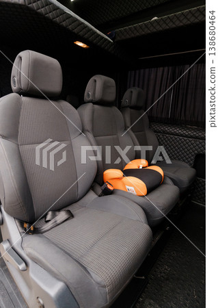 Interior view of empty gray upholstered passenger seats inside a black luxury shuttle van with orange accents. Interior view of empty gray upholstered passenger seats inside a black luxury shuttle van with orange accents. 138680464