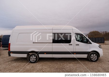 White commercial delivery van parked on gravel ground against a cloudy sky background. White commercial delivery van parked on gravel ground against a cloudy sky background. 138680465