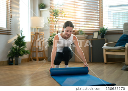 Woman folding, rolling exercise mat before working out at home. rolling Yoga mat after training healthy lifestyle Woman folding, rolling exercise mat before working out at home. rolling Yoga mat after training healthy lifestyle 138682270