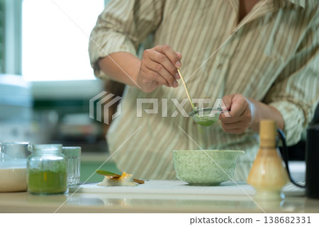 Cropped shot man hands sifting matcha powder into a traditional bowl for green tea preparation at kitchen home 138682331
