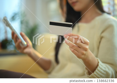 Closeup female holding credit card and smartphone at home doing shopping online transaction Closeup female holding credit card and smartphone at home doing shopping online transaction 138682336