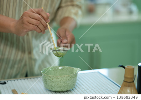 Cropped shot hands sifting matcha powder into a traditional bowl for green tea preparation at kitchen home Cropped shot hands sifting matcha powder into a traditional bowl for green tea preparation at kitchen home 138682349