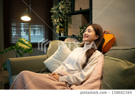 Relaxed woman using neck massager on sofa at home Relaxed woman using neck massager on sofa at home 138682384