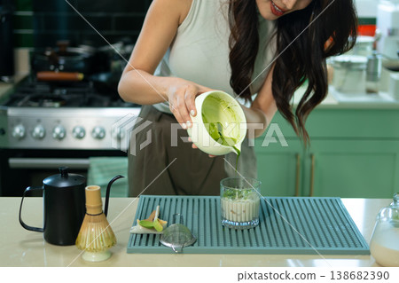 Cropped shot woman adding fresh matcha to glass of milk and ice for iced latte Cropped shot woman adding fresh matcha to glass of milk and ice for iced latte 138682390