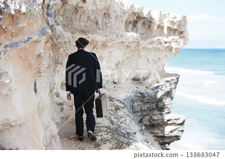 Businessman, thinking and walking with briefcase by ocean on ledge for mental health in back view. Person, anxiety or depression with mindset for difficulty in decision making in development space 138683047