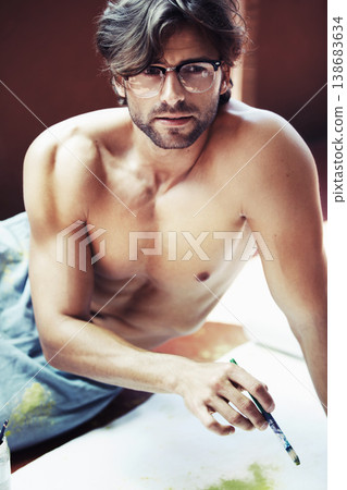 Portrait, man and glasses while serious with paintbrush for art project, hobby or work in space. Shirtless, artist and thinking of inspiration for canvas with paint for oil, acrylic or water colors Portrait, man and glasses while serious with paintbrush for art project, hobby or work in space. Shirtless, artist and thinking of inspiration for canvas with paint for oil, acrylic or water colors 138683634