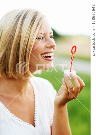 Happy woman, smile and blowing bubbles in nature for fun day in sunshine at outdoor park. Face of young female person or blonde with stick or wand to blow bubble on playful holiday or summer break Happy woman, smile and blowing bubbles in nature for fun day in sunshine at outdoor park. Face of young female person or blonde with stick or wand to blow bubble on playful holiday or summer break 138683648