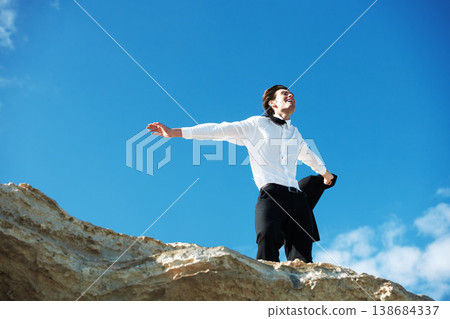 Cliff, freedom or happy business man in celebration of success or victory on holiday vacation. Sky background, goal or excited employee winner on mountain with achievement or job promotion in suit Cliff, freedom or happy business man in celebration of success or victory on holiday vacation. Sky background, goal or excited employee winner on mountain with achievement or job promotion in suit 138684337