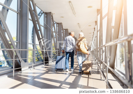 Rear view of mature couple walking in airport terminal with luggage Rear view of mature couple walking in airport terminal with luggage 138686810