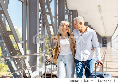 Mature couple walking through modern airport corridor with rolling suitcases Mature couple walking through modern airport corridor with rolling suitcases 138686811