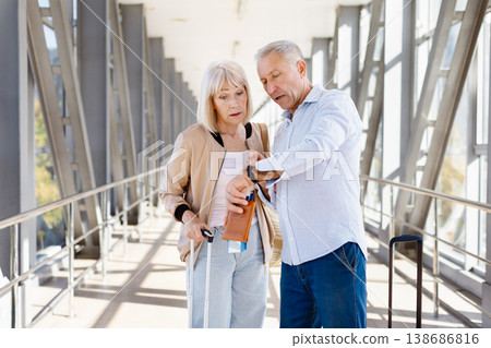Mature couple at airport terminal checking time and travel documents Mature couple at airport terminal checking time and travel documents 138686816