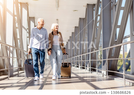 Happy mature couple walking hand in hand in airport terminal with luggage Happy mature couple walking hand in hand in airport terminal with luggage 138686826