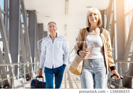 Mature couple leading walk through bright airport corridor with luggage Mature couple leading walk through bright airport corridor with luggage 138686835