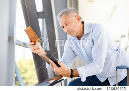 Mature man holding passport and smartphone in airport, checking travel information Mature man holding passport and smartphone in airport, checking travel information 138686855