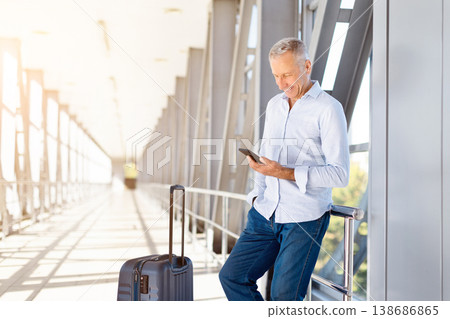 Mature man using smartphone in airport terminal while standing with luggage 138686865