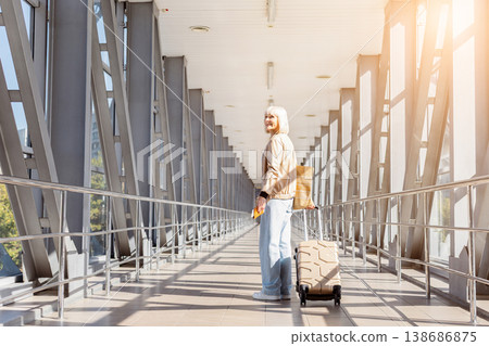 Mature woman standing in airport terminal with suitcase and passport, looking back 138686875