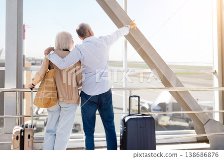 Mature couple standing together at airport window, man pointing toward runway Mature couple standing together at airport window, man pointing toward runway 138686876