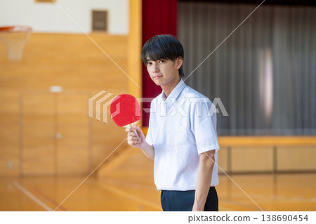 A male student holding a table tennis racket in the gymnasium. 138690454