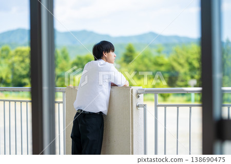 一名高中男生正站在教學大樓的陽台上向窗外眺望。 138690475