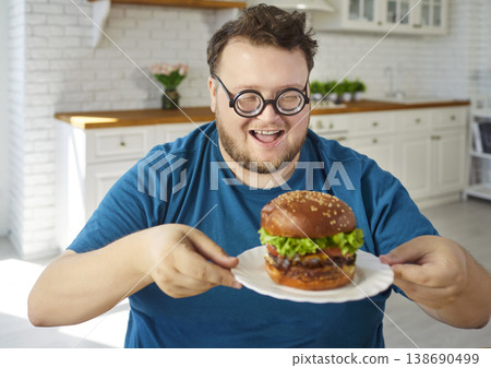 Overweight happy man with glasses enjoying burger at home kitchen with funny smile 138690499