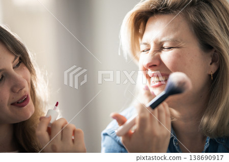 Daughter applying makeup on laughing mother's face 138690917
