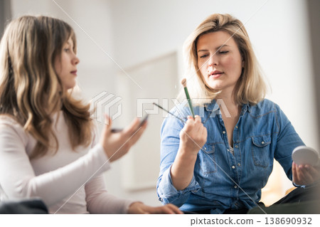 Woman holding makeup brushes looking at cosmetic products Woman holding makeup brushes looking at cosmetic products 138690932