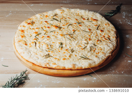Traditional Italian focaccia bread with melted cheese and fresh rosemary needles served on a rustic wooden board with flour. Traditional Italian focaccia bread with melted cheese and fresh rosemary needles served on a rustic wooden board with flour. 138691010
