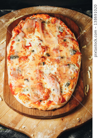 Traditional Italian pinsa romana with melted mozzarella gorgonzola cheese and slices of speck ham on a rustic wooden board. 138691020