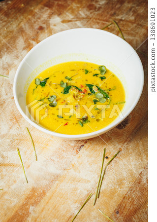 Gourmet pumpkin soup or cream of vegetable soup garnished with fresh microgreens and herbs served in a white ceramic bowl on a rustic wooden table. 138691023