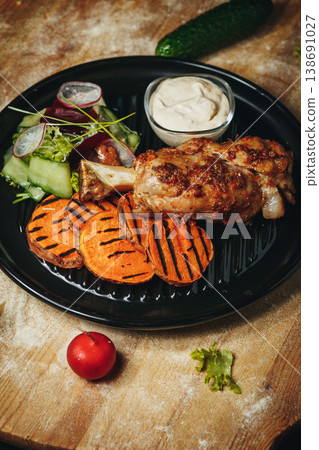 Roasted pork knuckle served with grilled sweet potato slices a fresh garden salad and creamy dipping sauce on a black plate. Roasted pork knuckle served with grilled sweet potato slices a fresh garden salad and creamy dipping sauce on a black plate. 138691027