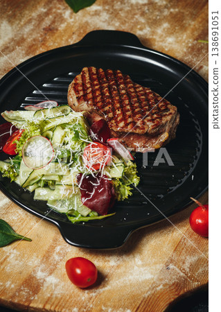Gourmet grilled beef steak with perfect char marks served with a fresh garden salad of cucumber cherry tomatoes and parmesan on a black grill pan. 138691051