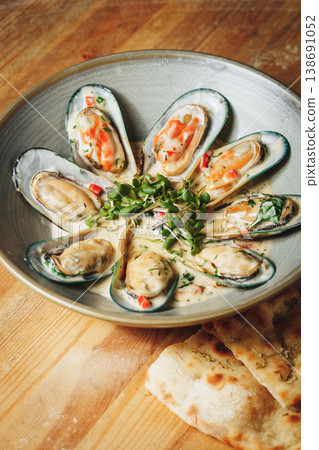 Gourmet green mussels in creamy white wine sauce garnished with fresh microgreens and red chili served in a ceramic bowl with flatbread. 138691052