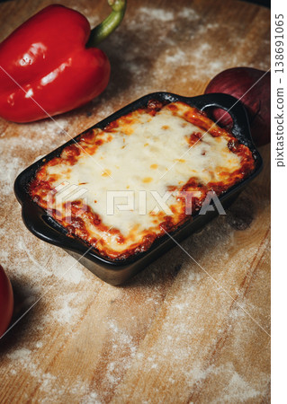 Traditional Italian beef lasagna with melted mozzarella cheese in a black ceramic baking dish on a rustic floured wooden table. Traditional Italian beef lasagna with melted mozzarella cheese in a black ceramic baking dish on a rustic floured wooden table. 138691065
