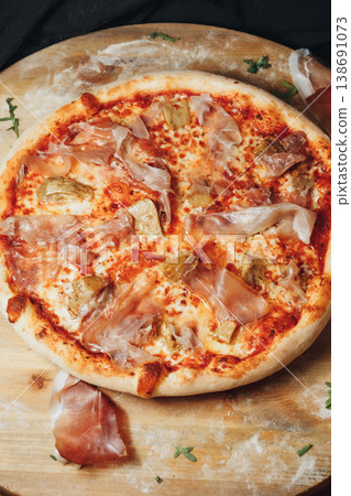 Traditional Italian pinsa romana topped with tomato sauce melted mozzarella artichoke hearts and thin slices of prosciutto ham on a wooden board. Traditional Italian pinsa romana topped with tomato sauce melted mozzarella artichoke hearts and thin slices of prosciutto ham on a wooden board. 138691073