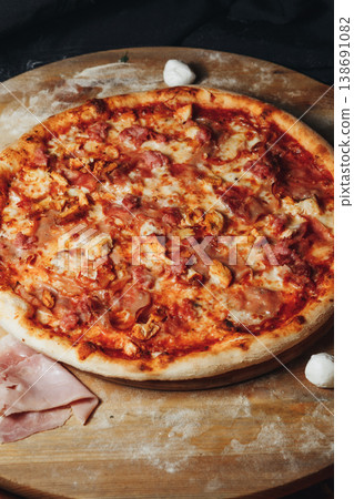 Authentic Italian pizza topped with tomato sauce melted mozzarella savory ham and prosciutto slices on a rustic wooden board with flour. 138691082