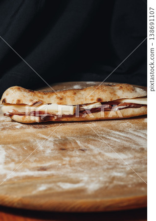 Traditional Italian saltimbocca sandwich made with artisanal pizza dough bread and thin slices of roasted meat on a floured wooden surface. Traditional Italian saltimbocca sandwich made with artisanal pizza dough bread and thin slices of roasted meat on a floured wooden surface. 138691107