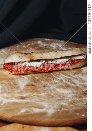 Gourmet artisanal flatbread sandwich filled with spicy salami and creamy blue cheese served on a rustic floured wooden board. Gourmet artisanal flatbread sandwich filled with spicy salami and creamy blue cheese served on a rustic floured wooden board. 138691119