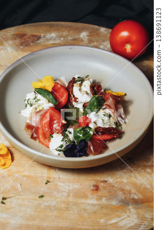 Gourmet Italian Caprese salad with fresh burrata cheese prosciutto ham cherry tomatoes and pesto sauce garnished with edible flowers. 138691123