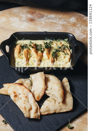 Gourmet shrimps in creamy garlic sauce garnished with fresh microgreens served in a black ceramic dish with toasted flatbread. Gourmet shrimps in creamy garlic sauce garnished with fresh microgreens served in a black ceramic dish with toasted flatbread. 138691124