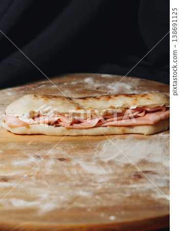 Traditional Italian piadina sandwich filled with thin slices of mortadella ham and creamy cheese served on a rustic floured wooden board. 138691125