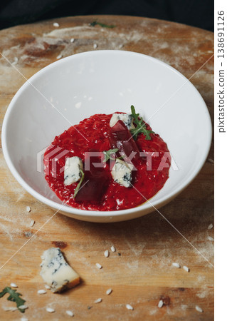 Gourmet beetroot risotto with a vibrant red color topped with creamy gorgonzola blue cheese and fresh microgreens in a white ceramic bowl. 138691126