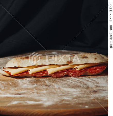 Artisanal pepperoni and cheese sandwich made with Italian saltimbocca bread served on a rustic floured wooden board. Artisanal pepperoni and cheese sandwich made with Italian saltimbocca bread served on a rustic floured wooden board. 138691128